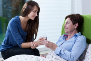 caregiver serving a glass of water to an elderly woman in bed